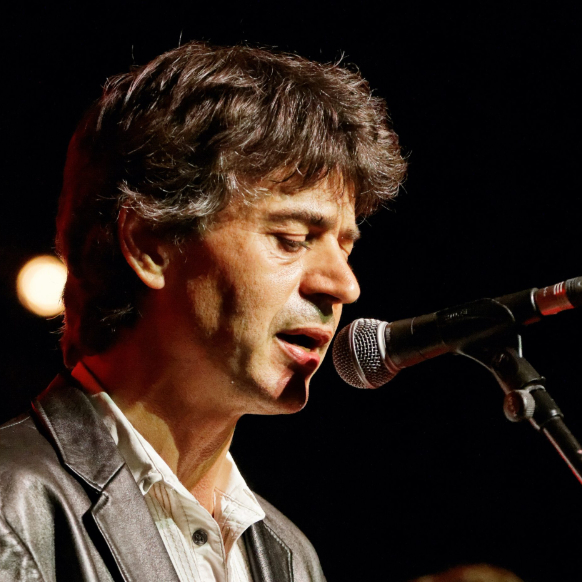 Denez Prigent from the side while he is singing on a live stage.
